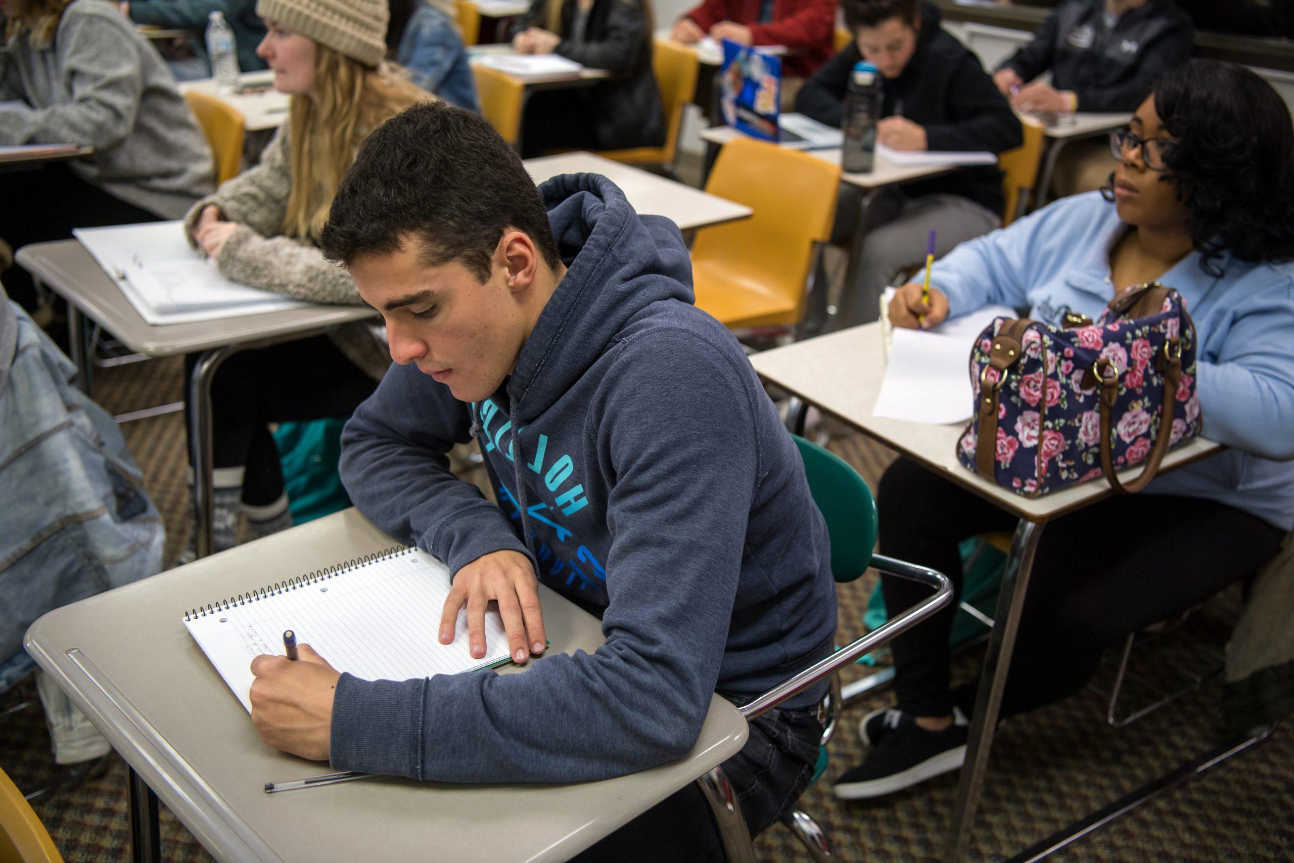 Athletic male student taking notes in class.