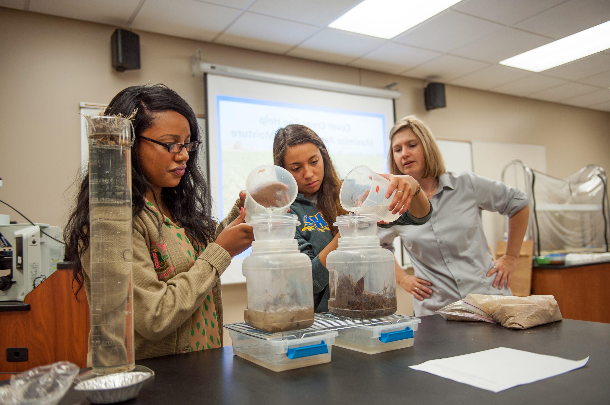 Two students with an instructor conducting a soil and water experiment in class.