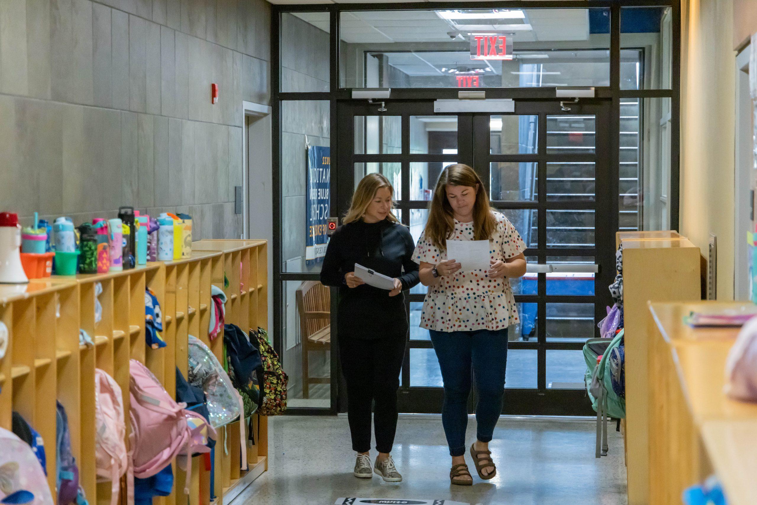 Two administrators walking down a school hallway while reviewing notes their holding in their hands.